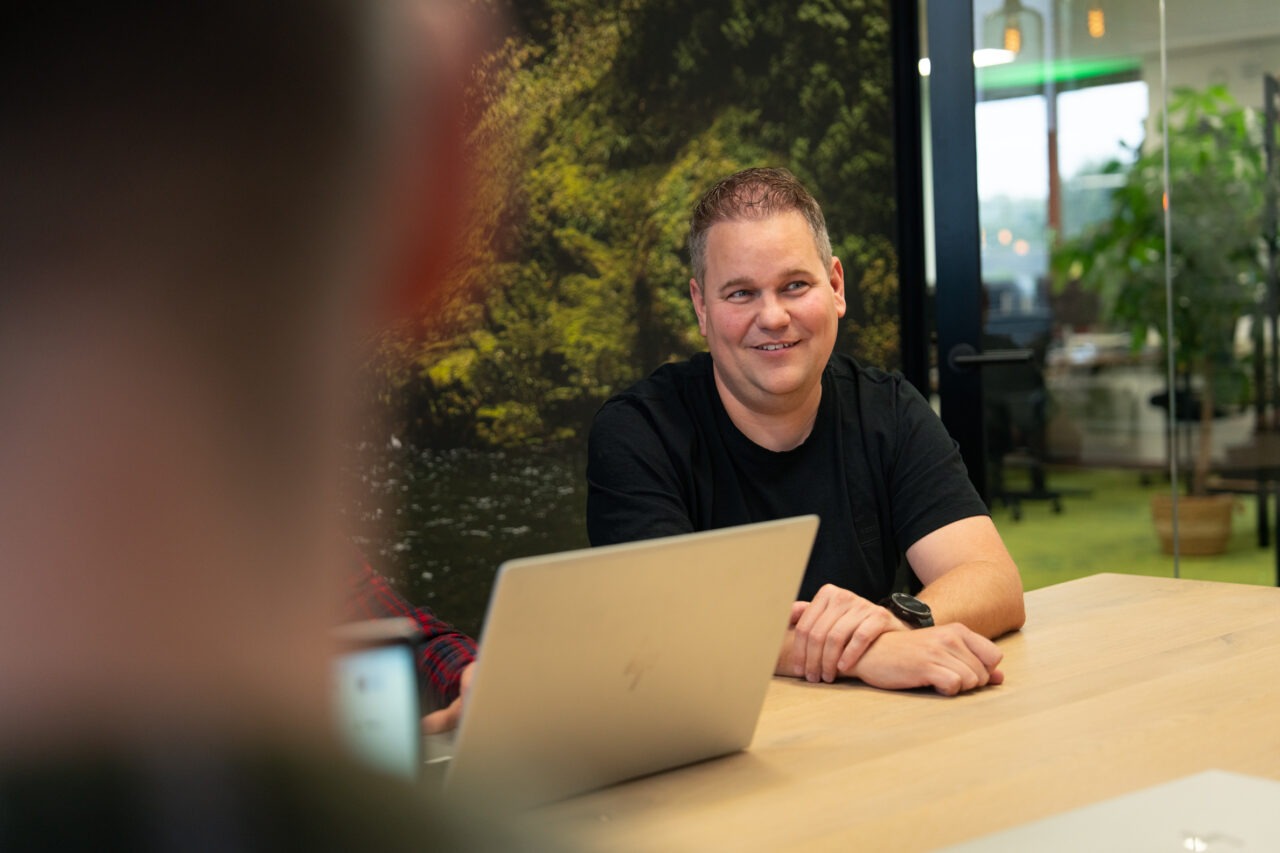 Een consultant van Wux AI zit glimlachend aan een houten vergadertafel met een laptop tijdens een strategisch adviesgesprek over de AVG en AI-wetgeving.