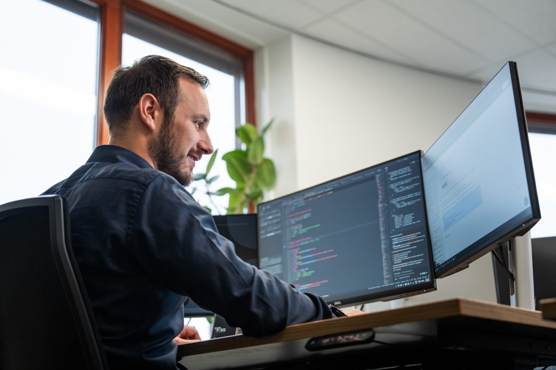 Een ontwikkelaar van Wux AI kijkt lachend naar schermen met code, wat staat voor de slimme integratie van AI-tools bij MKB-bedrijven.